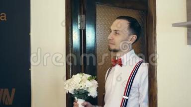 在门口，年轻人进来了，新郎，戴着红色的蝴蝶结，带着<strong>一束花</strong>。 他看着新娘。